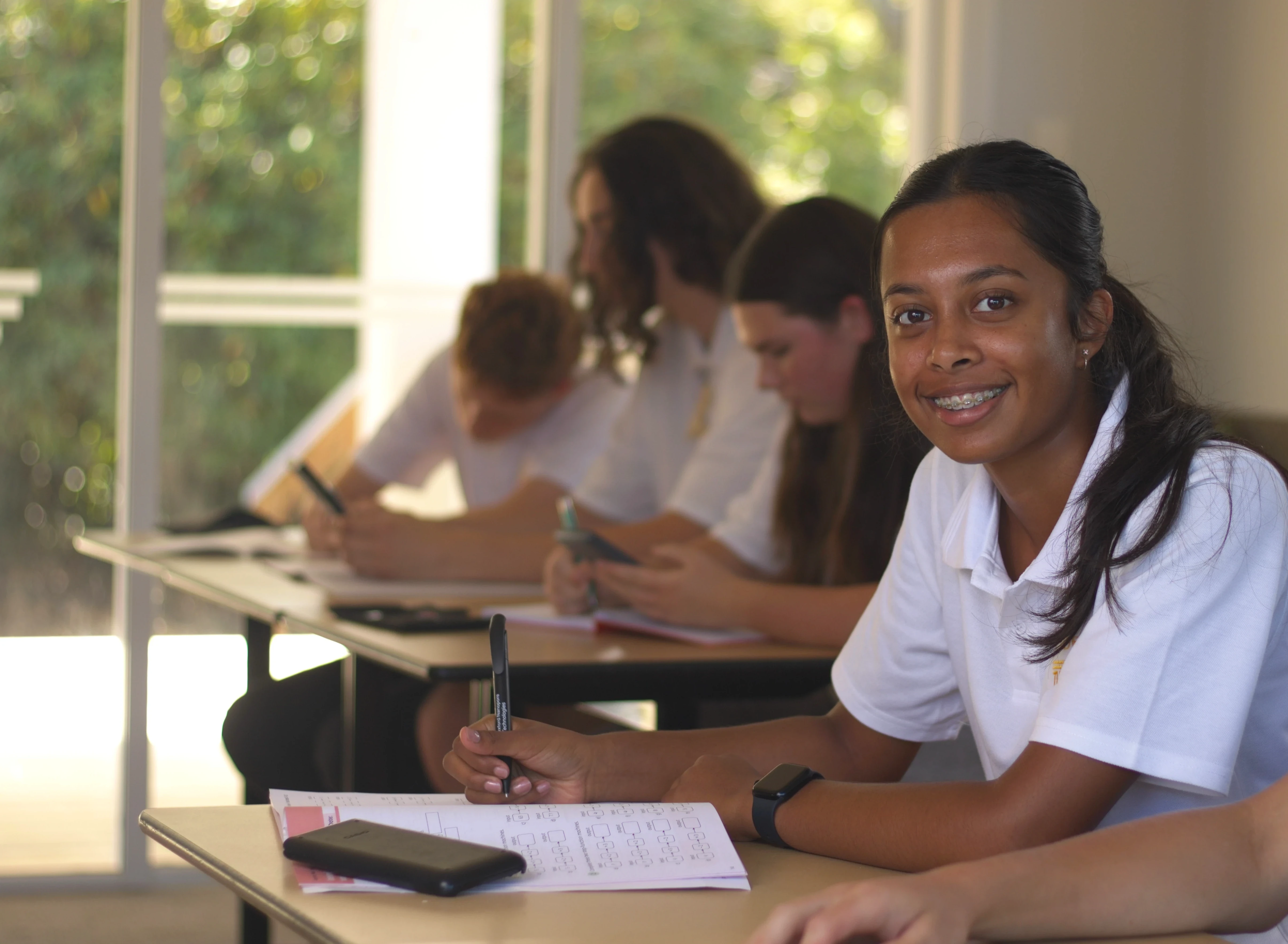 A student enrolled at The Academy in the middle of writing and smiling at the camera